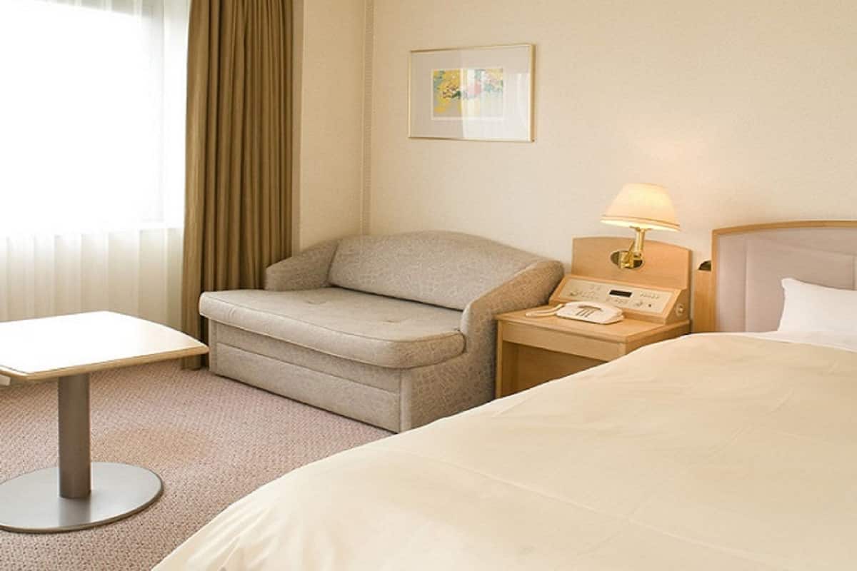 A hotel room with a bed, a sofa, a small table, a nightstand with a lamp, and a painting on the wall.