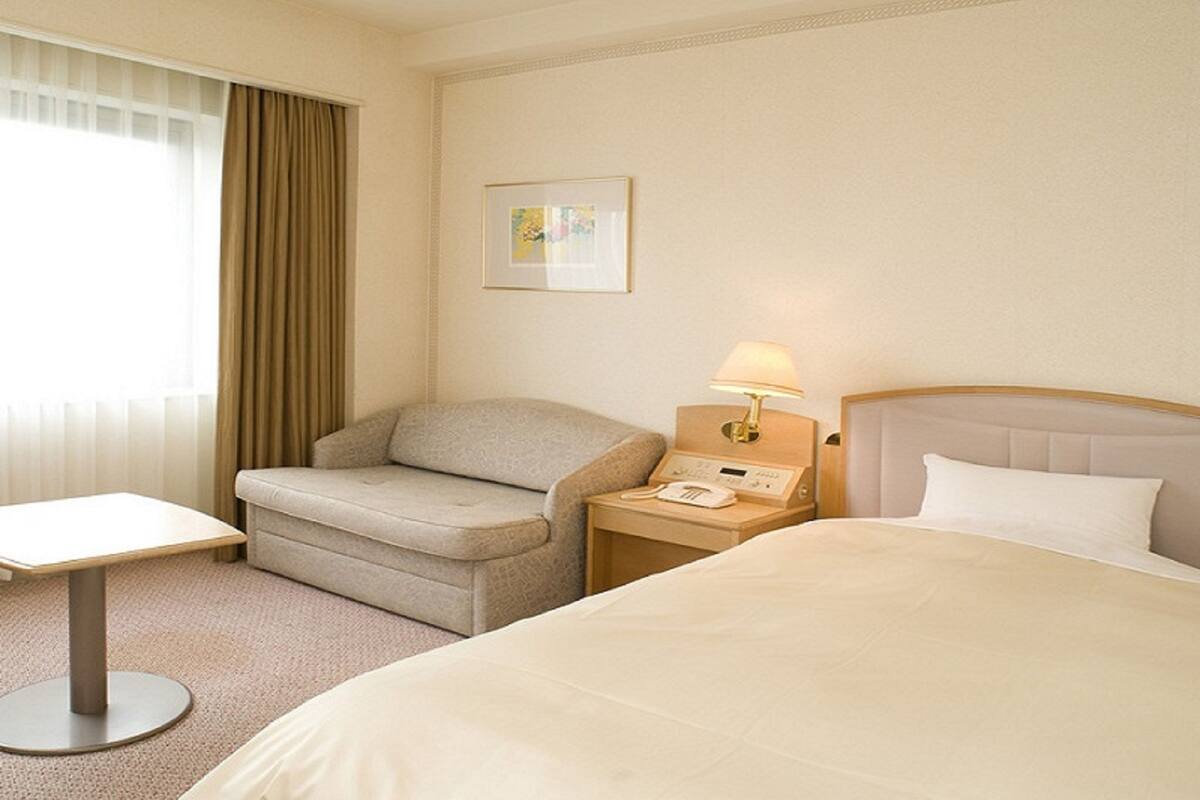 A hotel room with a bed, a sofa, a small table, a lamp, and a picture on the wall.