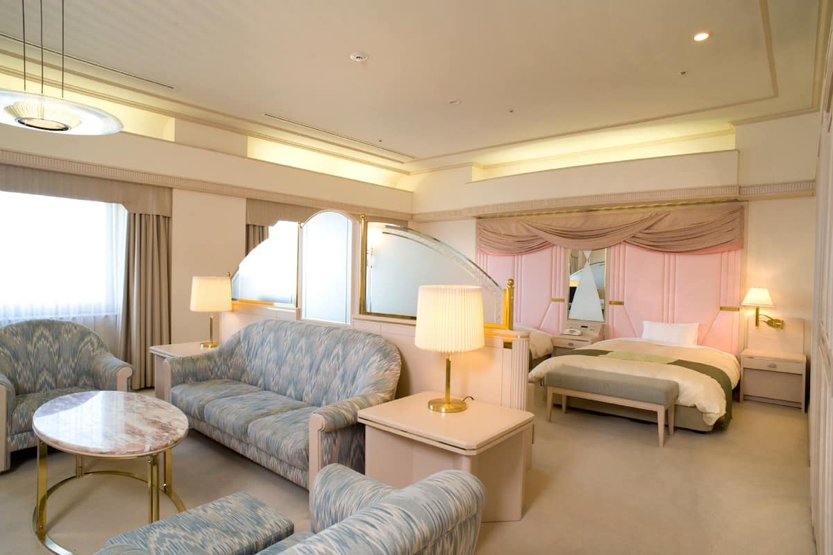 A hotel room with a bed, two armchairs, a small table, and a bedside table with lamps.