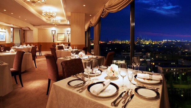 A dining area with tables set for a meal, large windows with a city view, and chandeliers. - Rihga Royal Hotel Niihama (Niihama)
