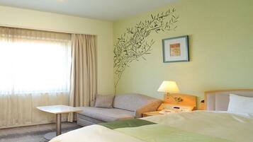 A hotel room with a bed, a sofa, a small table, and a lamp.