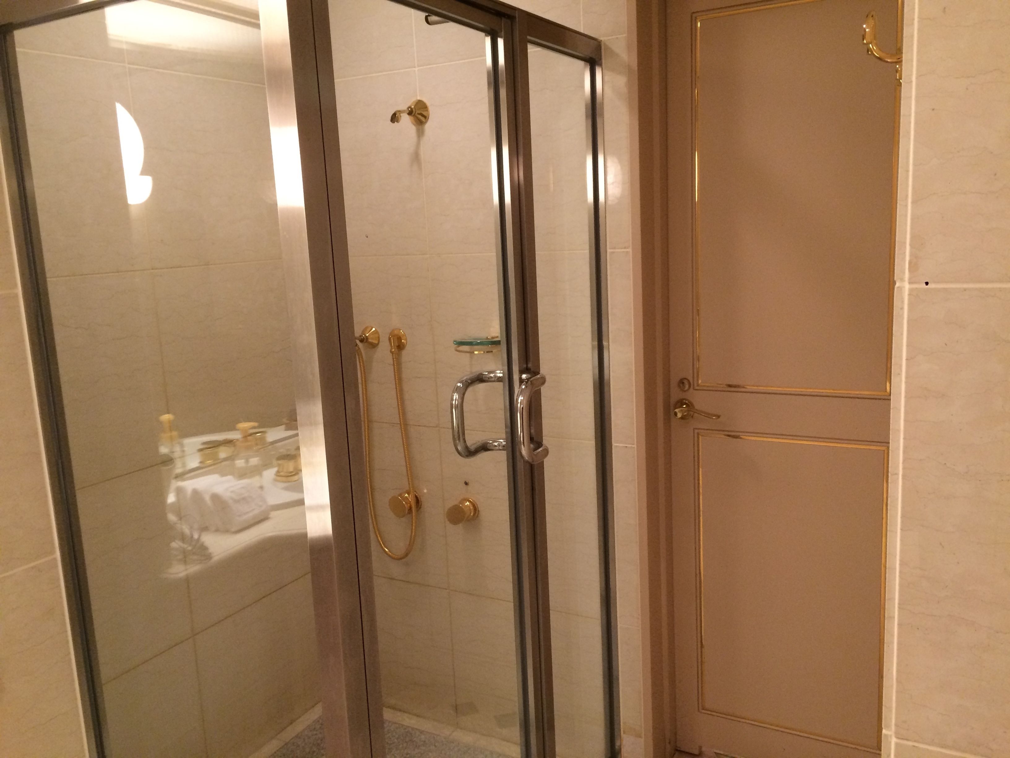 Une douche fermée par des parois de verre, dotée d’accessoires dorés et d’une étagère en verre.