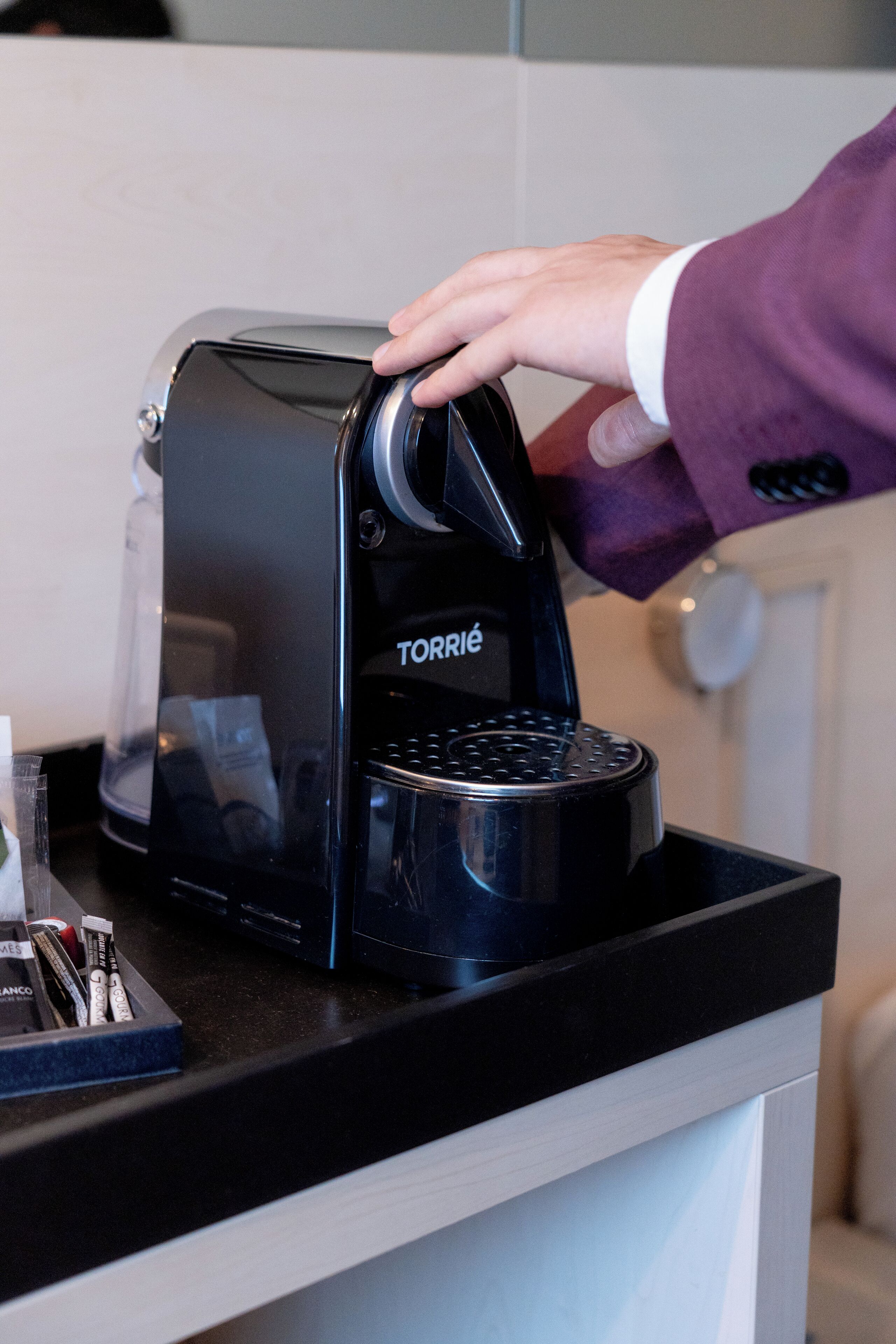 A person operating a black coffee machine labeled "TORRIÉ" on a countertop.