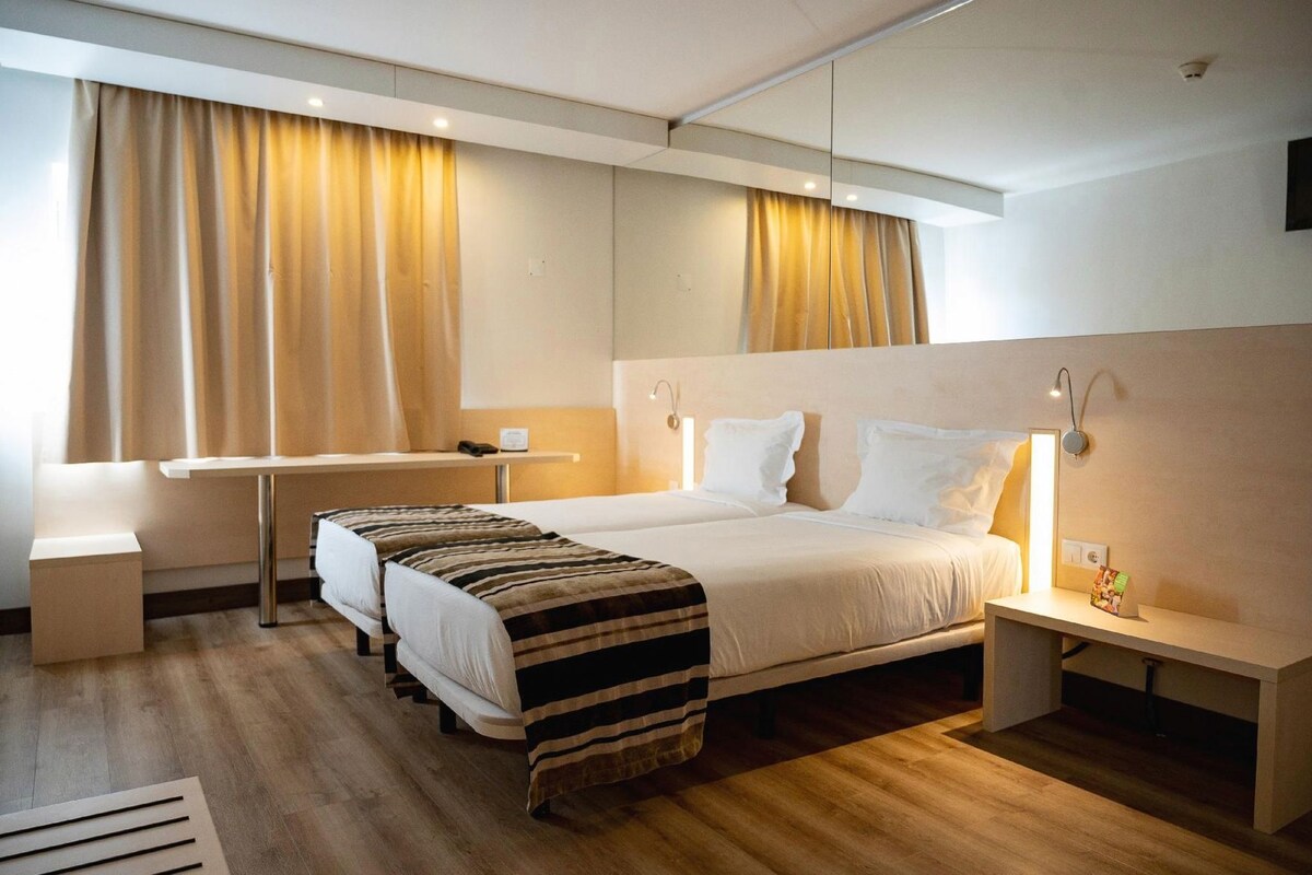 A hotel room with a bed, bedside tables, a desk, and curtains.