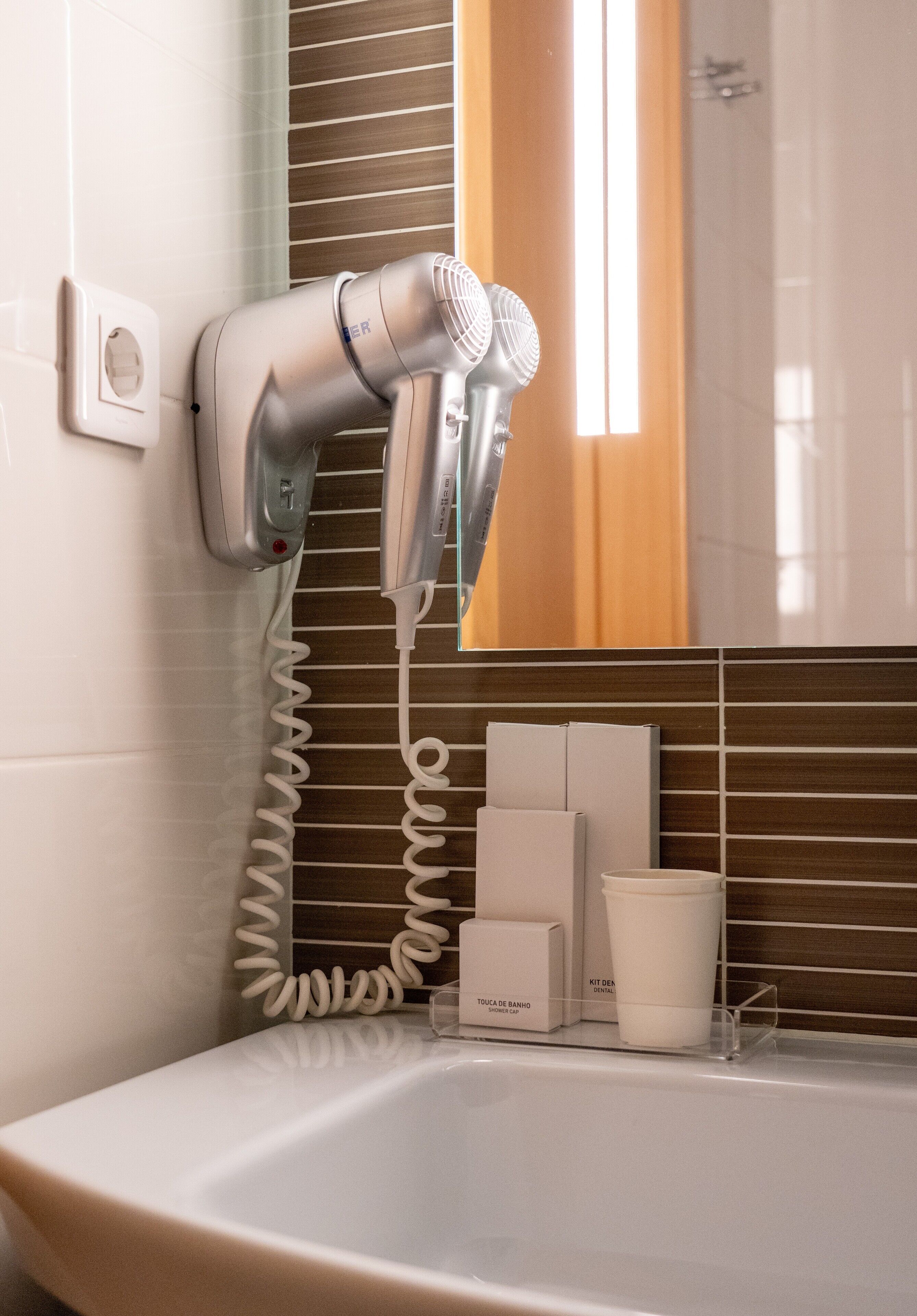 A bathroom with a hairdryer mounted on the wall, a bathtub, and toiletries on the counter.
