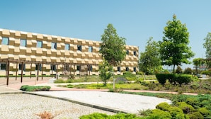A modern building with a geometric facade, surrounded by a landscaped garden with various shrubs and trees.