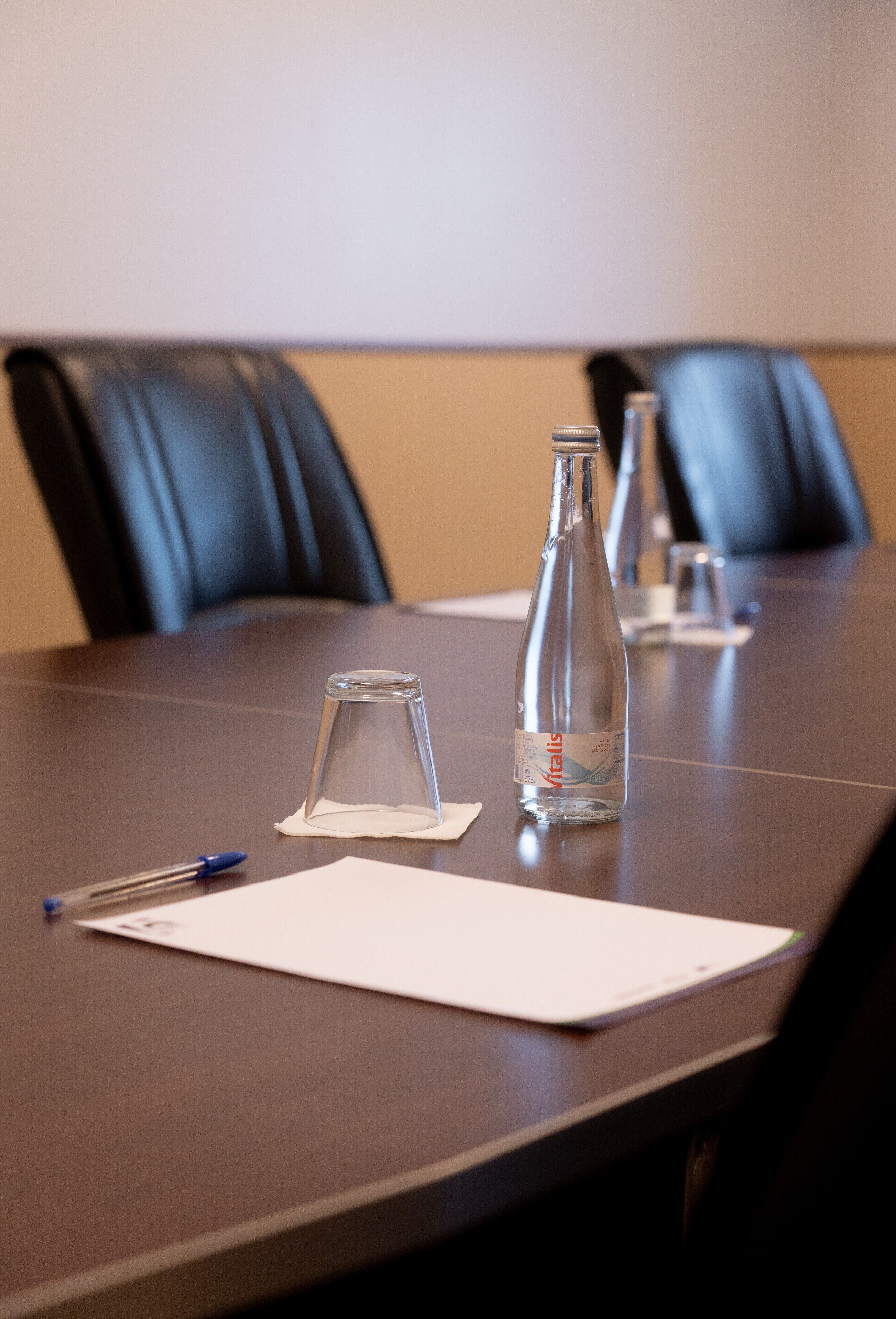 A conference table with a bottle of water, a glass, and a pen on it.