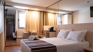A hotel room with a bed, bedside tables, a mirror, a window with curtains, and a door leading to a bathroom.