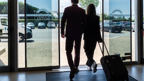 A hotel entrance with a glass door, a tiled floor, and a view of parked cars outside.
