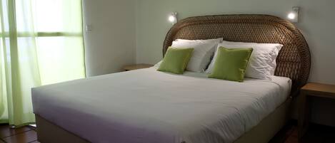 A bed with white and green pillows, a wicker headboard, and a bedside table with a lamp.