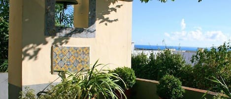 Un balcón con plantas en macetas, un muro de baldosas y vista al mar.