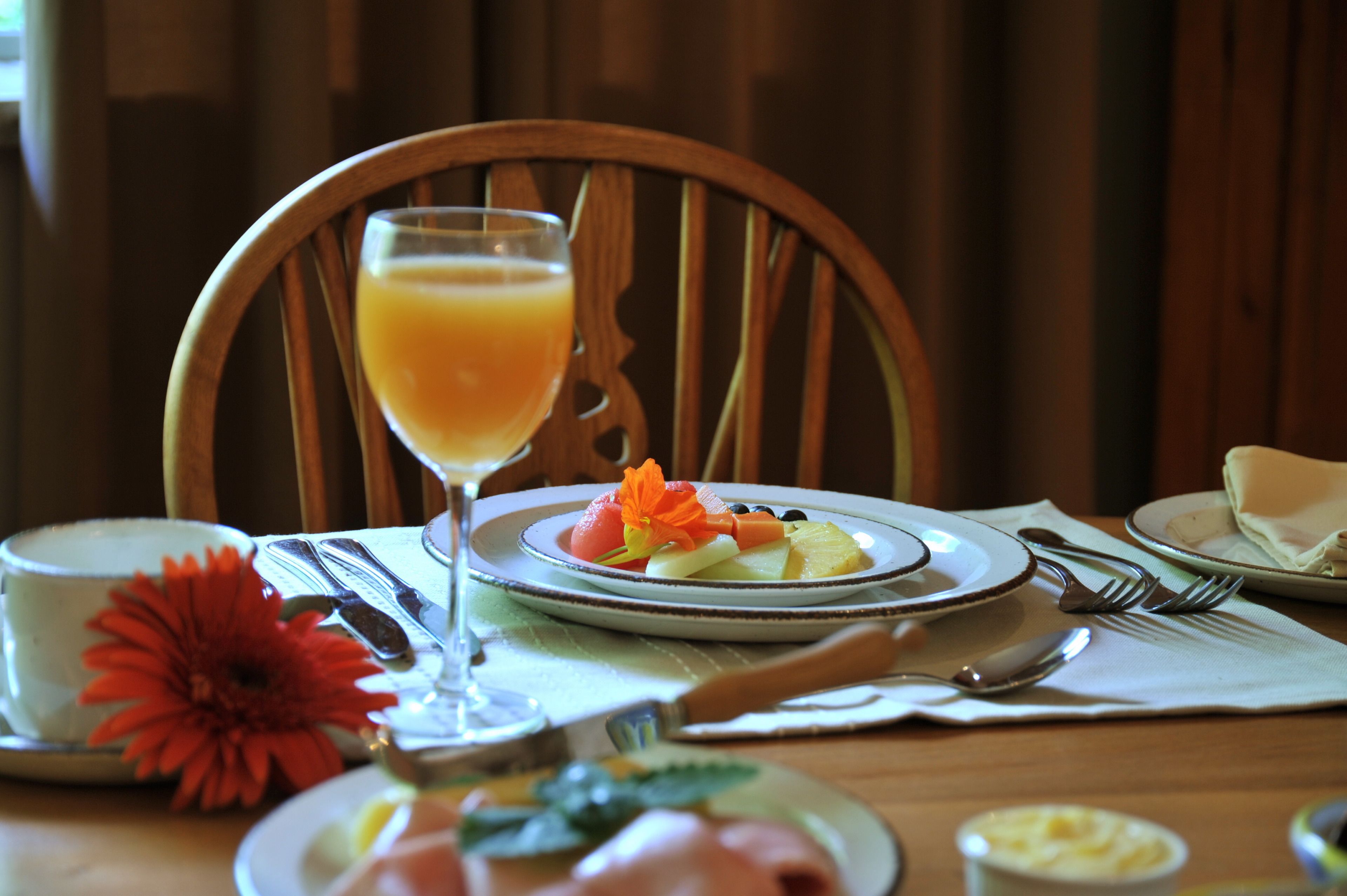 Morgenmadsbord med frugt, et glas appelsinjuice og en rød blomst på en træbordplade.