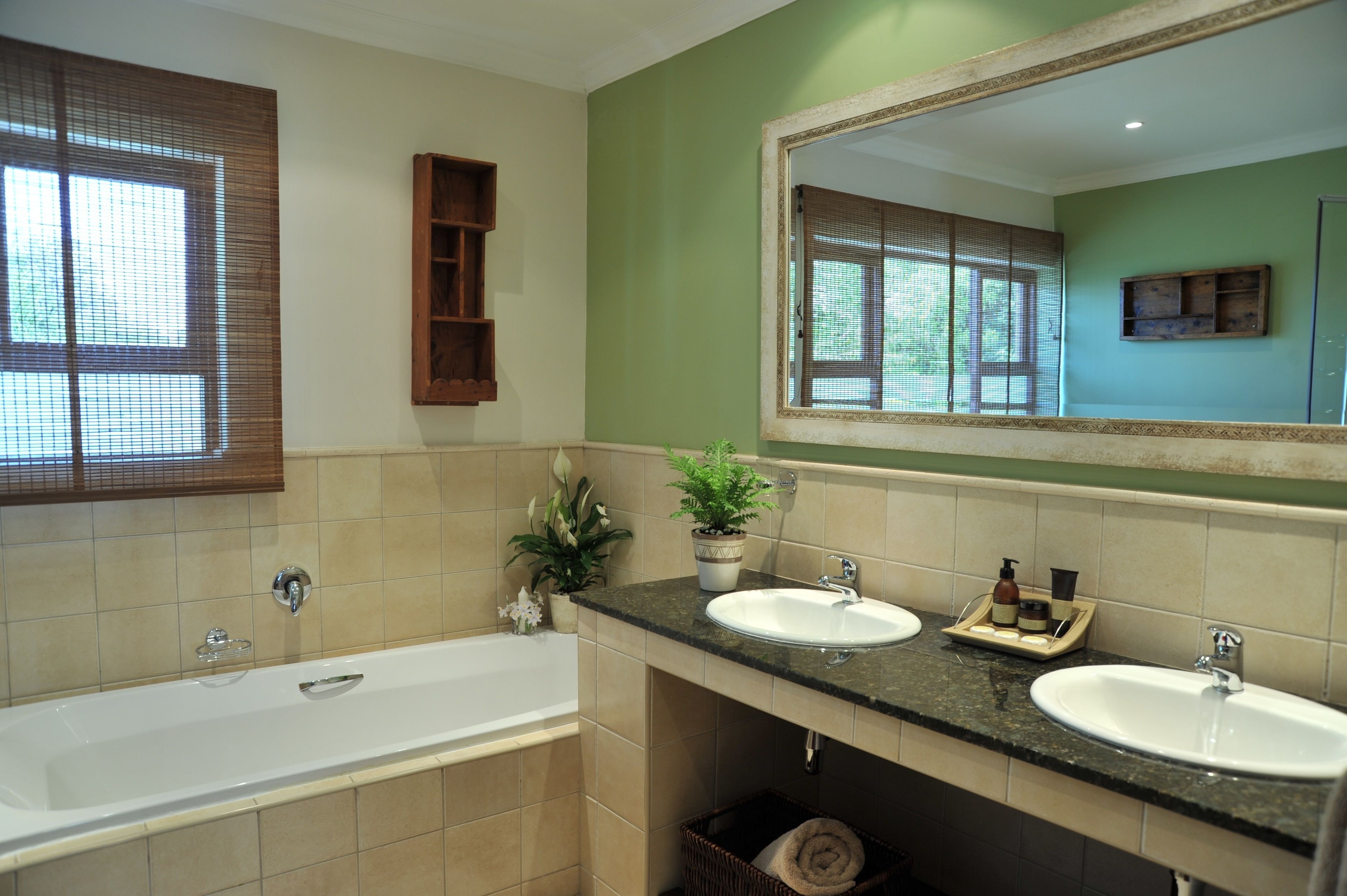 A bathroom with a bathtub, two sinks, a large mirror, and a window with blinds.
