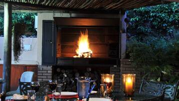 An outdoor dining area with a brick fireplace, tables, chairs, and candles.