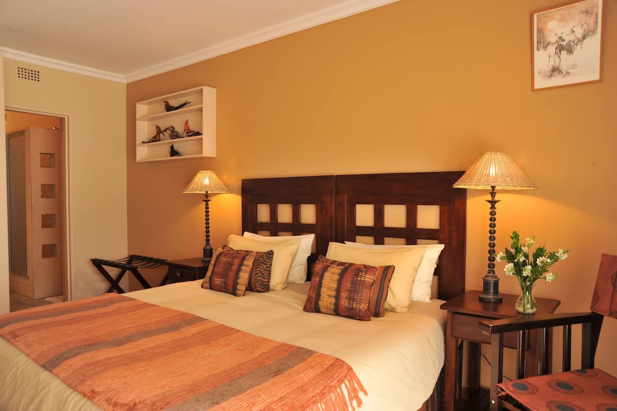 Habitación de hotel con una cama grande, dos lámparas de noche, una mesita con un jarrón de flores y un cabecero de madera.