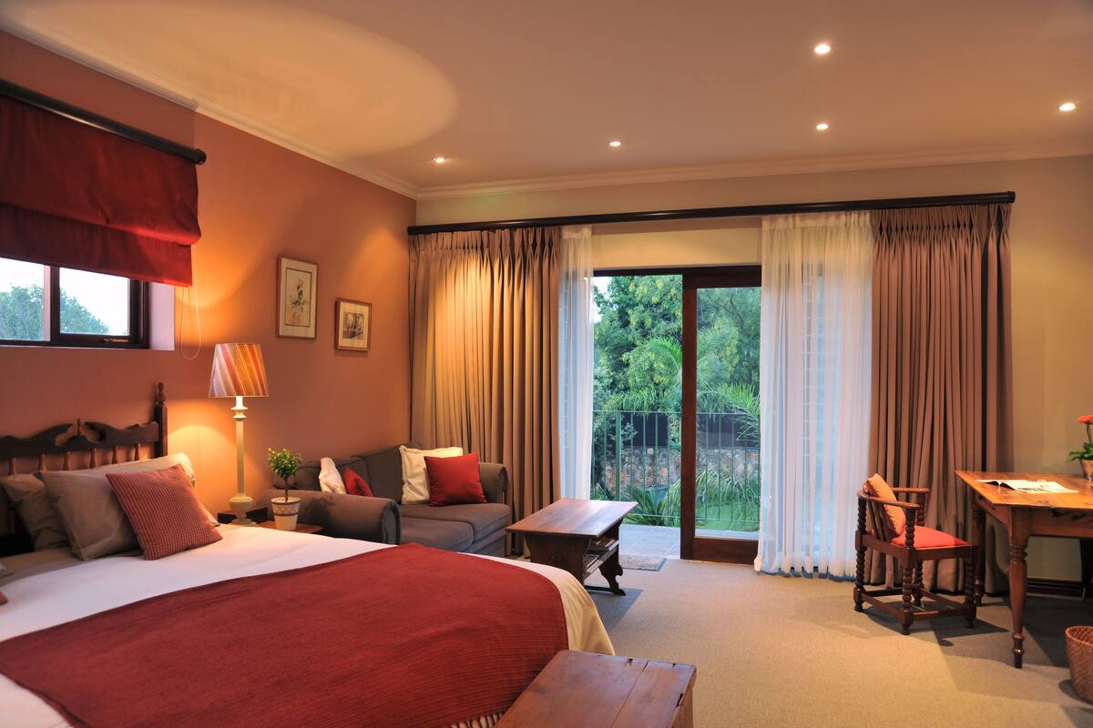 Habitación de hotel con una cama grande, un sofá, una mesa de comedor y vistas al exterior a través de un ventanal corredero.