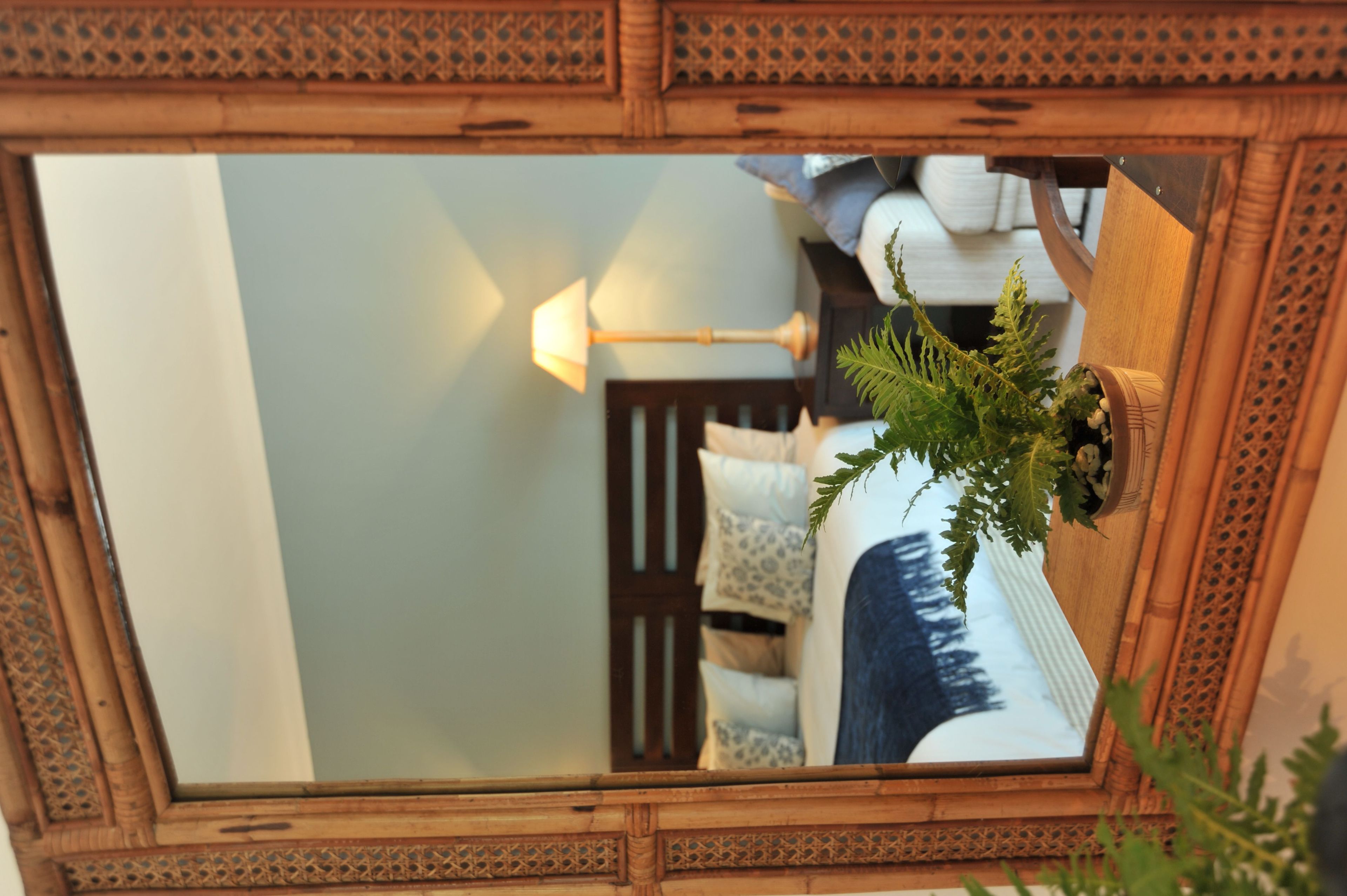 A mirror reflecting a room with a bed, pillows, a lamp, and a plant.