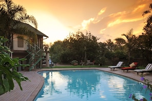 A swimming pool with lounge chairs, a staircase, and a building with a tiled roof. - Claires of Sandton (Sandton)