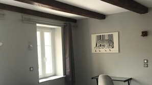 A bedroom with a bed, a desk, and a chair. There is a window with curtains, a zebra artwork on the wall, and exposed wooden beams on the ceiling. - Hôtel de la Basilique (Epinal)