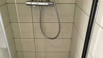 A glass-enclosed shower with a showerhead and a drain.