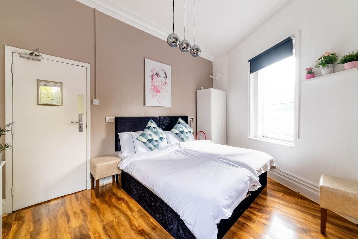 Une chambre à coucher avec un grand lit, une table de chevet, une armoire, une fenêtre donnant sur un beau paysage et une porte ornée d’un cadre de tableau.
