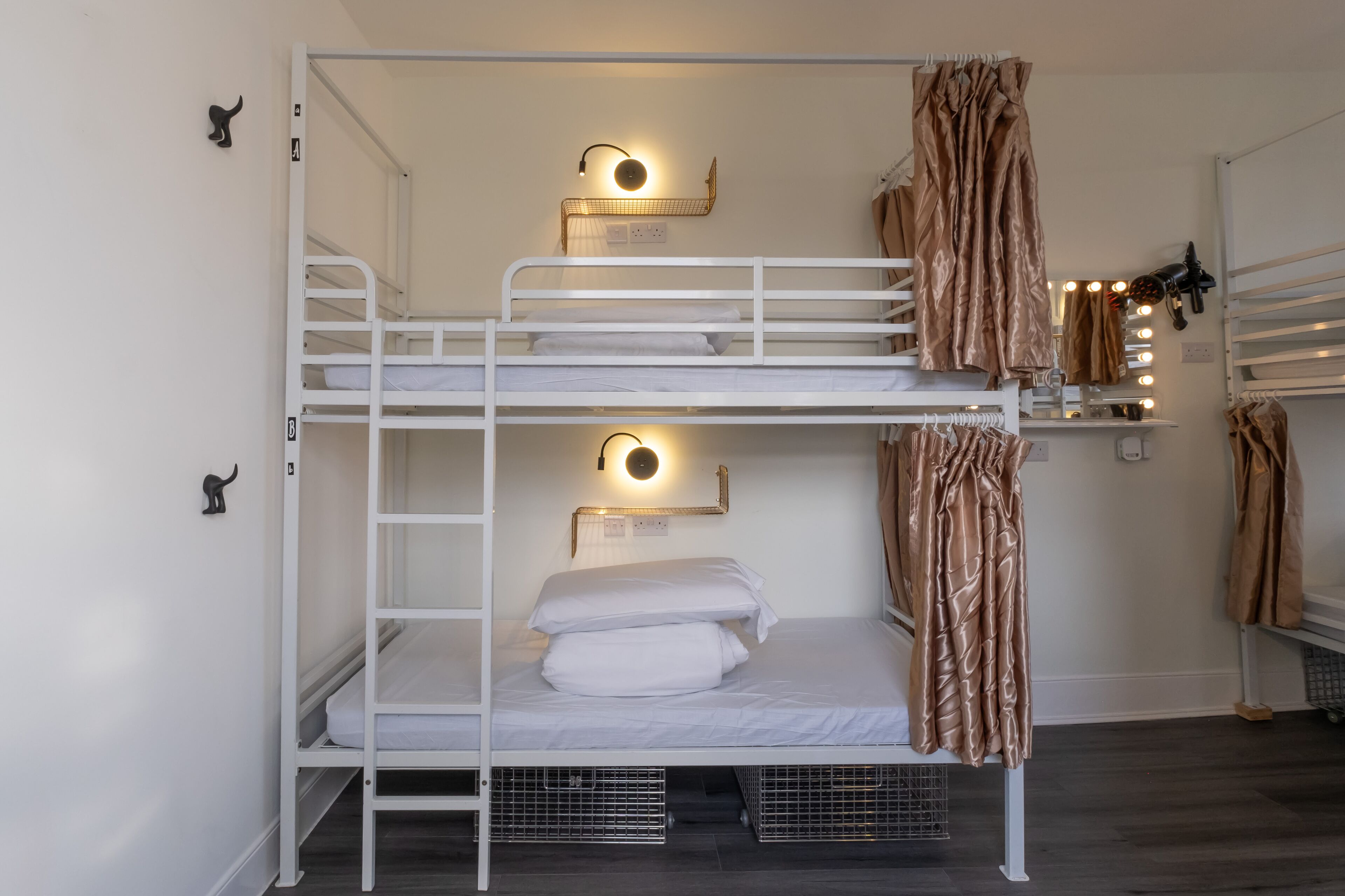 A bunk bed room with two levels, each with a wall-mounted light fixture. There are two metal storage bins under the lower bunk.