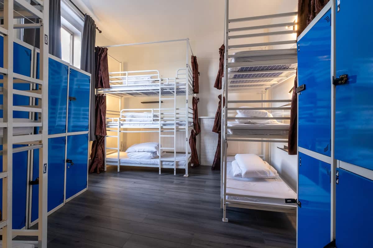 Une chambre de dortoir avec des lits superposés, des casiers bleus et un plancher en bois.