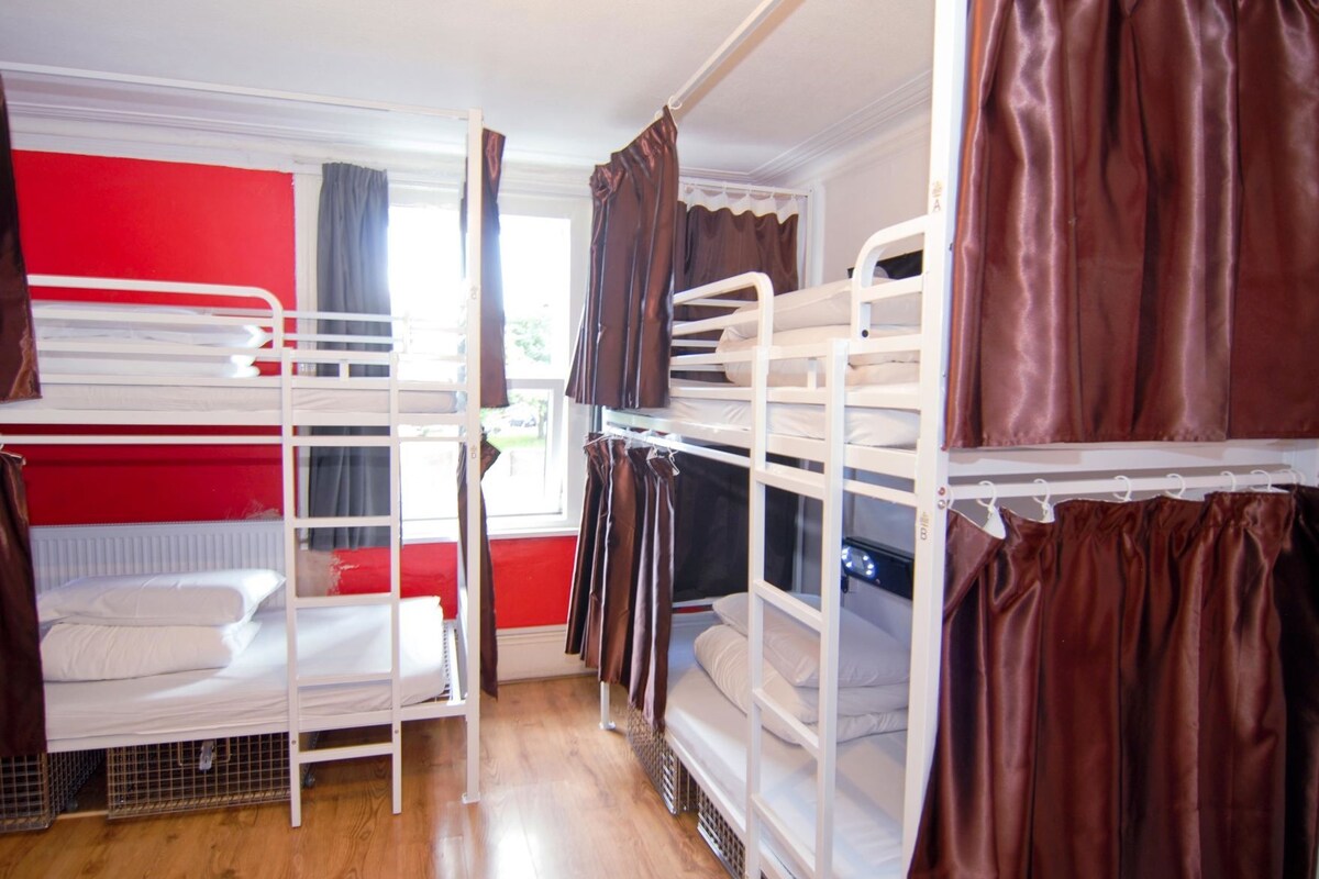 Quarto com beliche, parede vermelha, roupa de cama branca e cortinas castanhas.
