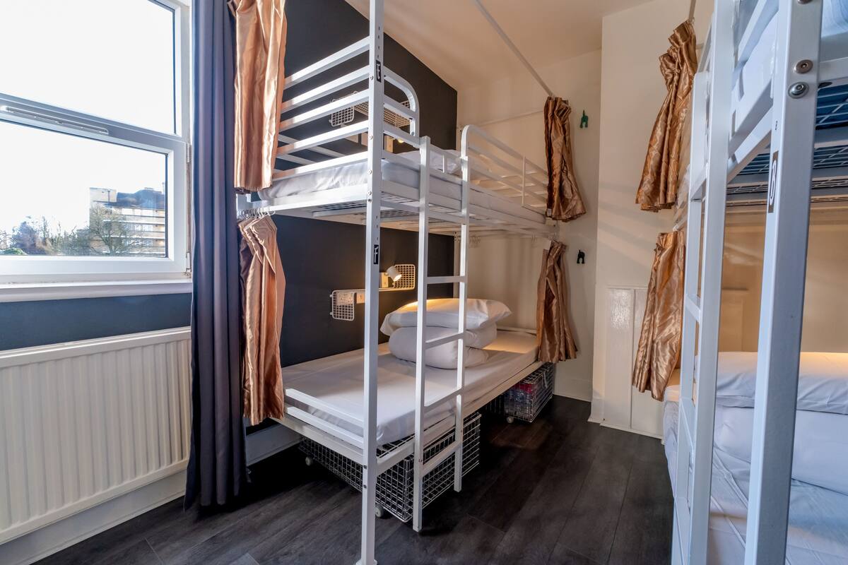 Une chambre avec un lit superposé, une fenêtre, des rideaux et un radiateur.