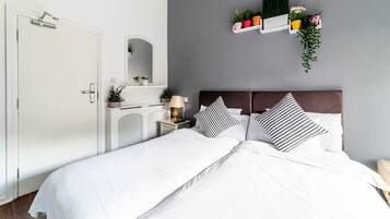 A neatly arranged bedroom with a bed, bedside tables, a mirror, and a wall-mounted shelf with plants.
