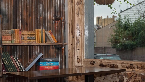 Una estantería rústica con libros y una cesta de flores colgante.