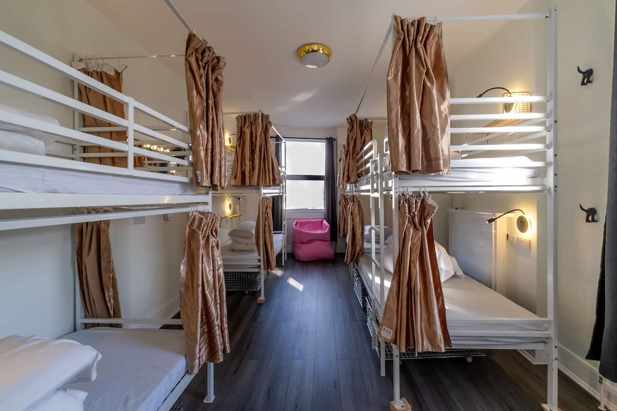 Une chambre avec plusieurs lits superposés, un fauteuil-pouf rose et une fenêtre laissant entrer la lumière naturelle.