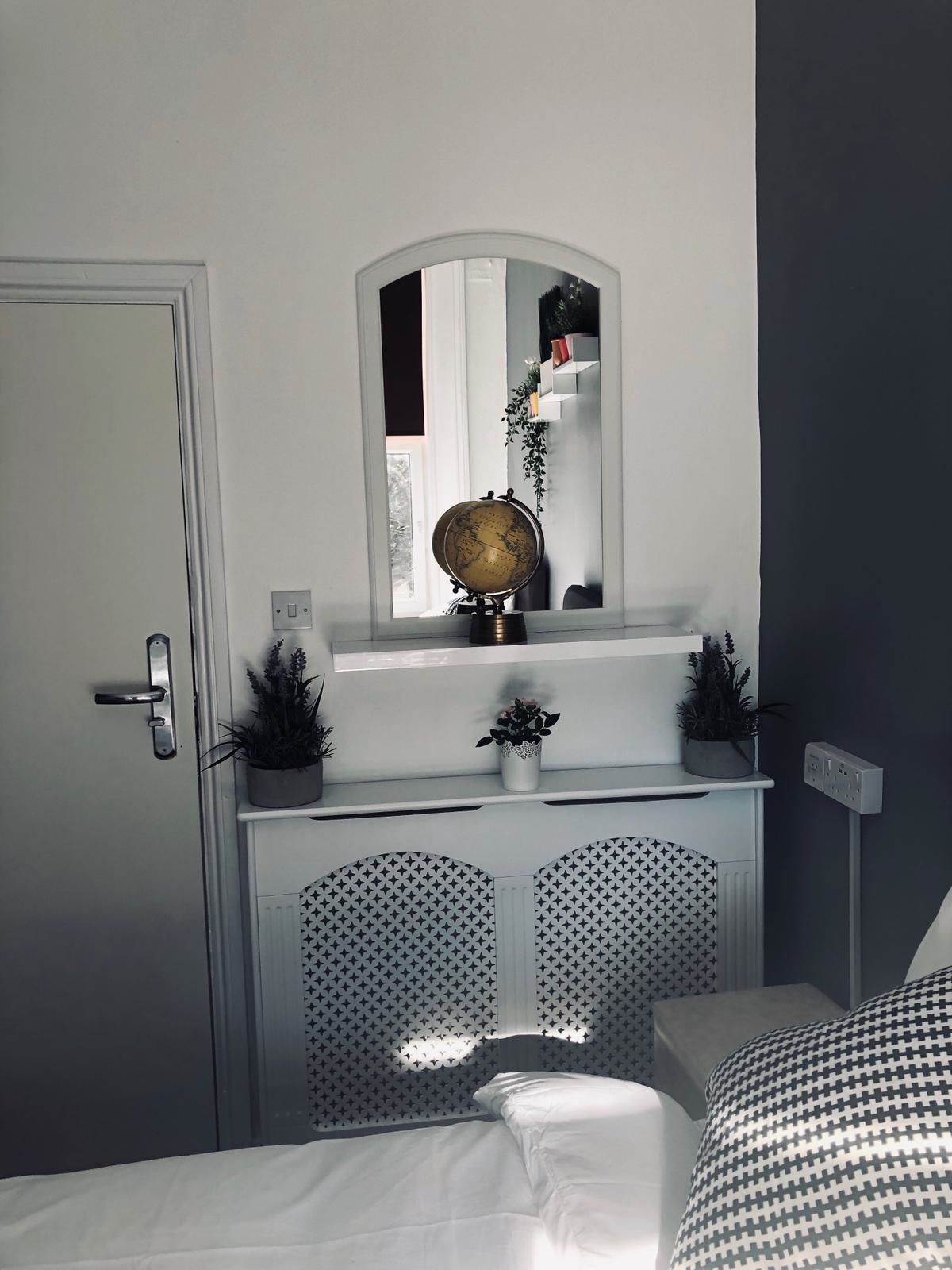 Une chambre à coucher avec un lit, une commode avec un miroir, un globe terrestre et des plantes en pot.