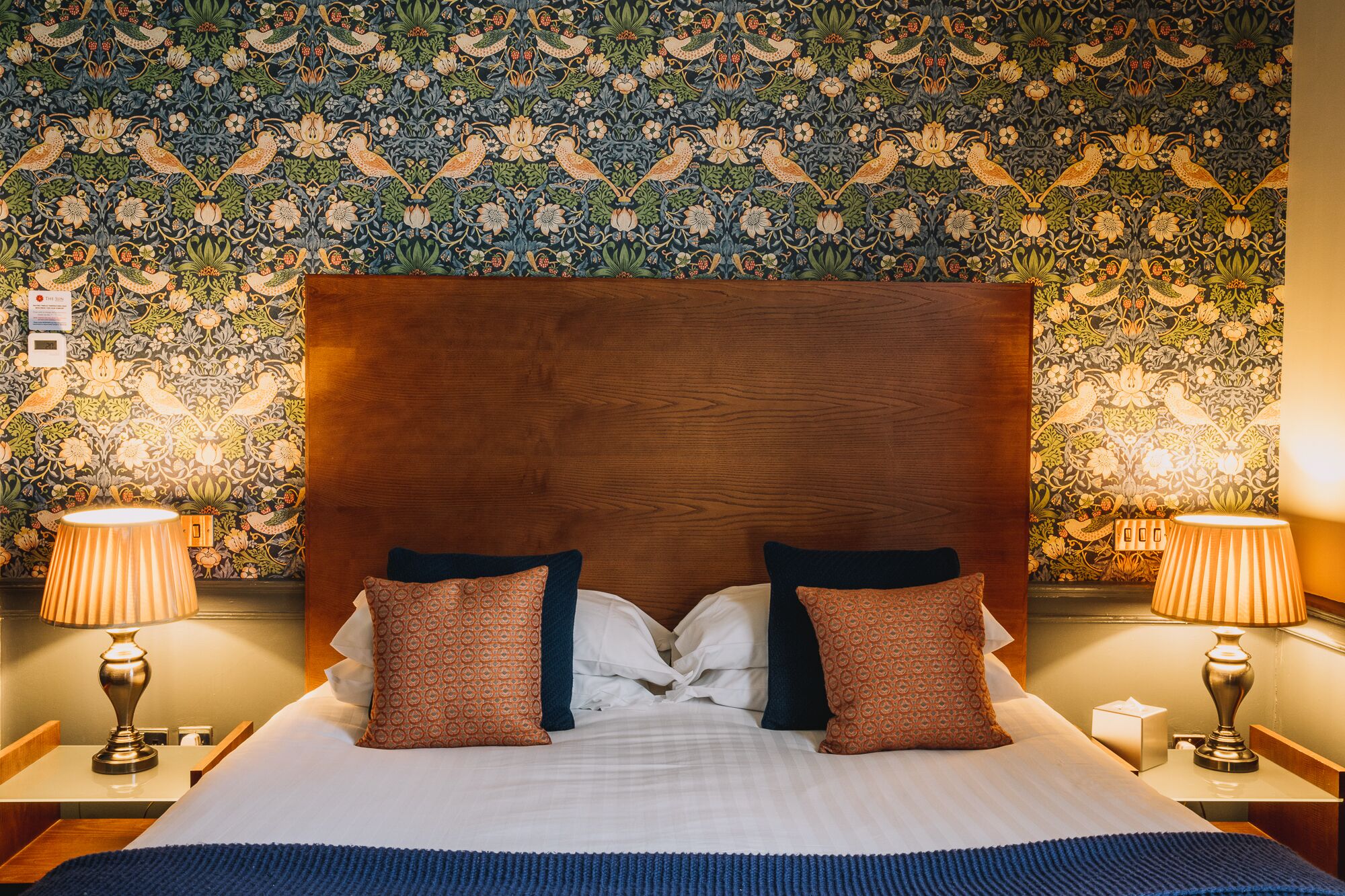 A hotel room with a large bed, two nightstands, and a wall with a floral pattern.