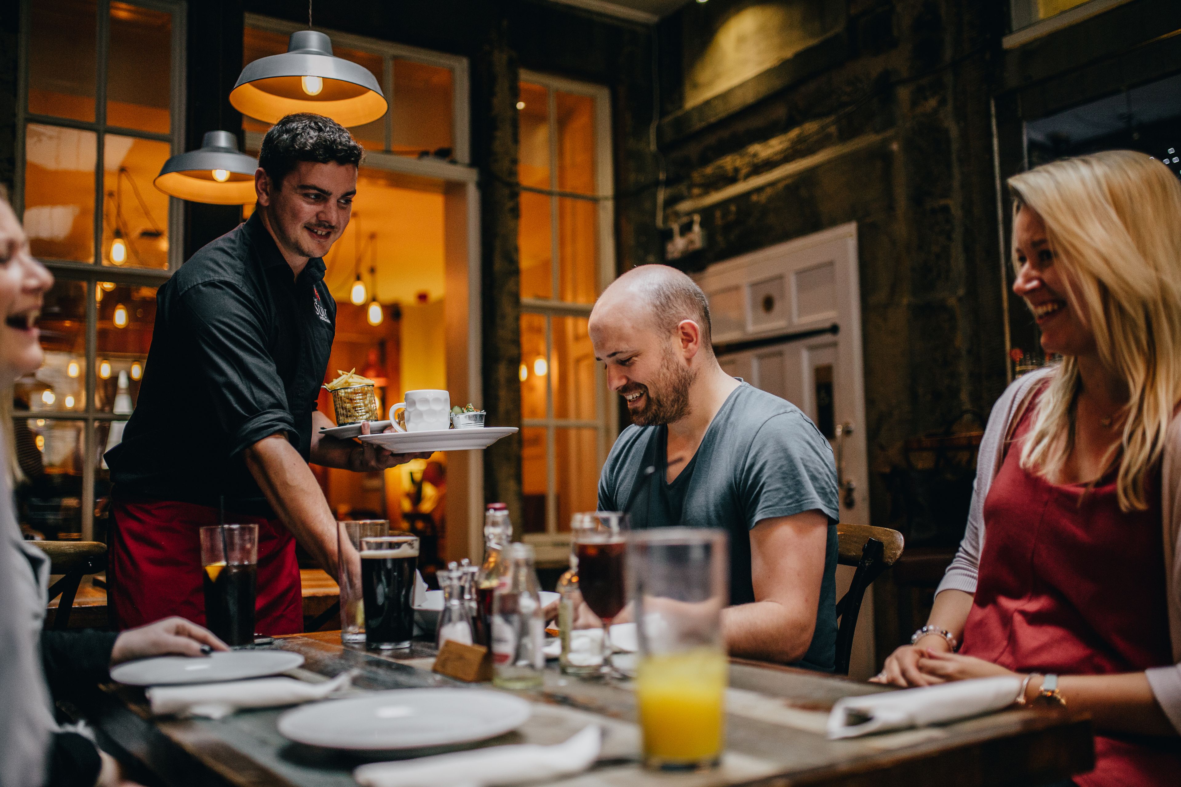 A restaurant with a wooden interior, a waiter serving a table, and diners.