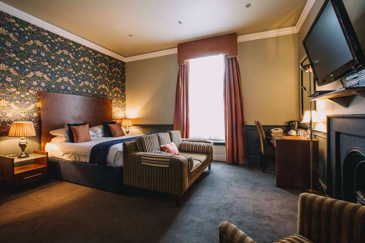 A hotel room with a bed, a sofa, a television, and a fireplace.