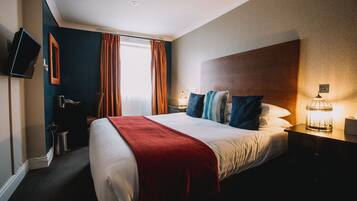 Quarto de hotel com uma cama grande, televisão na parede, mesa de cabeceira com abajur e janela com cortinas.