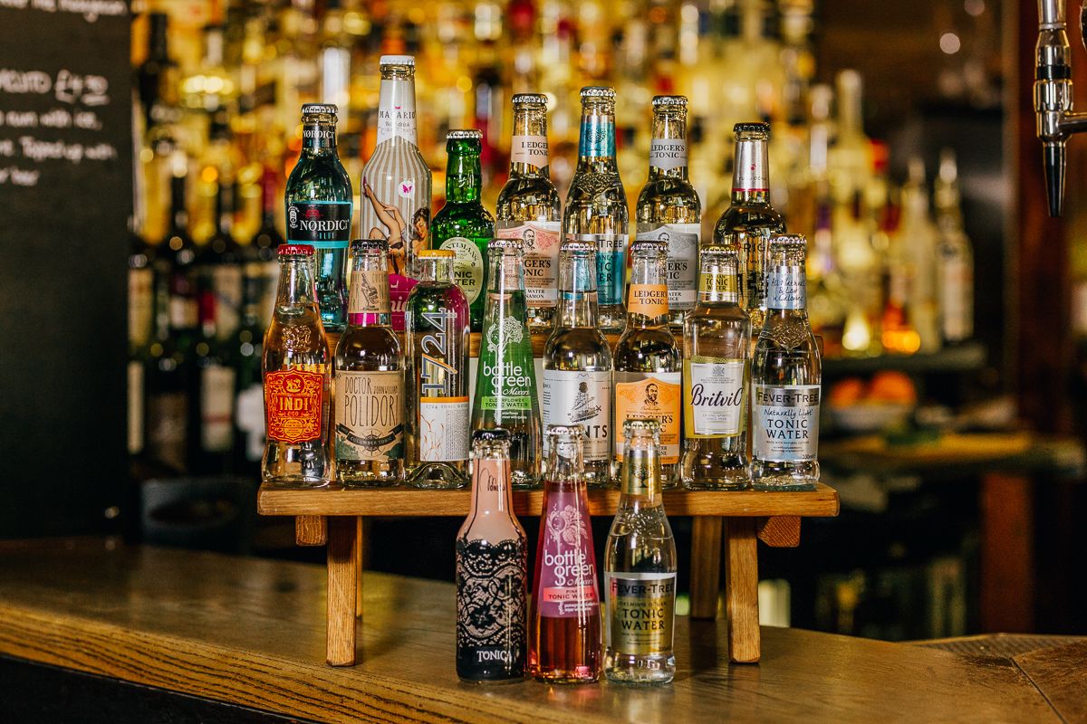 A variety of liquor bottles displayed on a wooden stand at a bar.