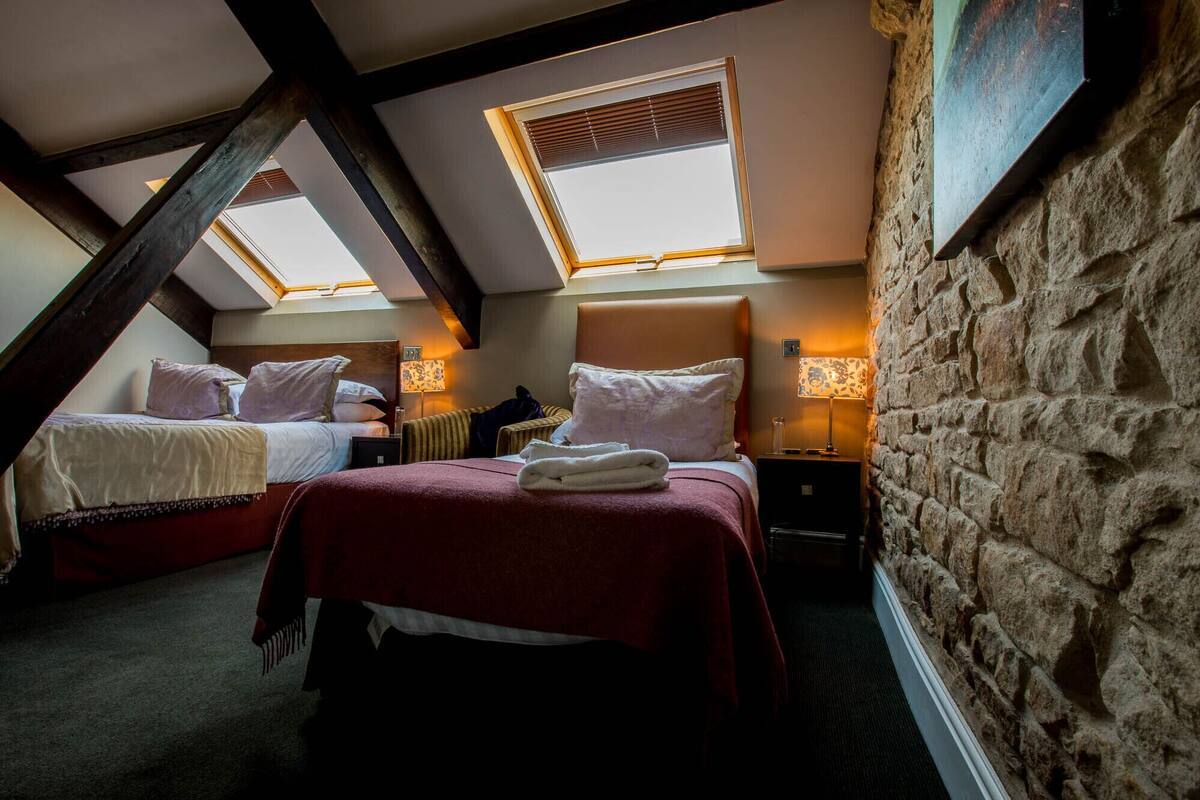 A cozy attic bedroom with two beds, a stone wall, and skylights.