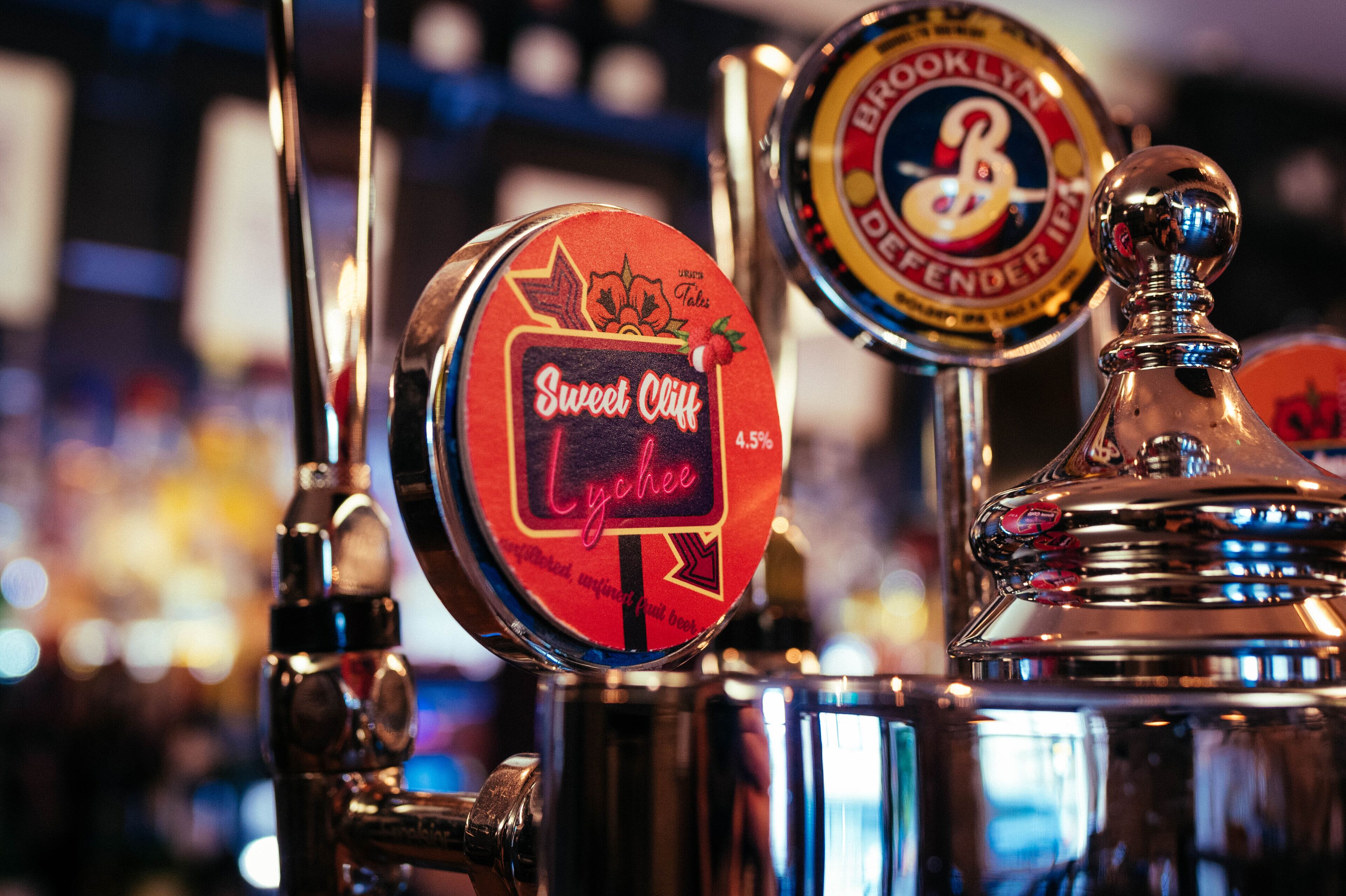 Un primo piano di rubinetti per birra con le etichette 'Sweet Cliff' e 'Brooklyn Defender IPA'.