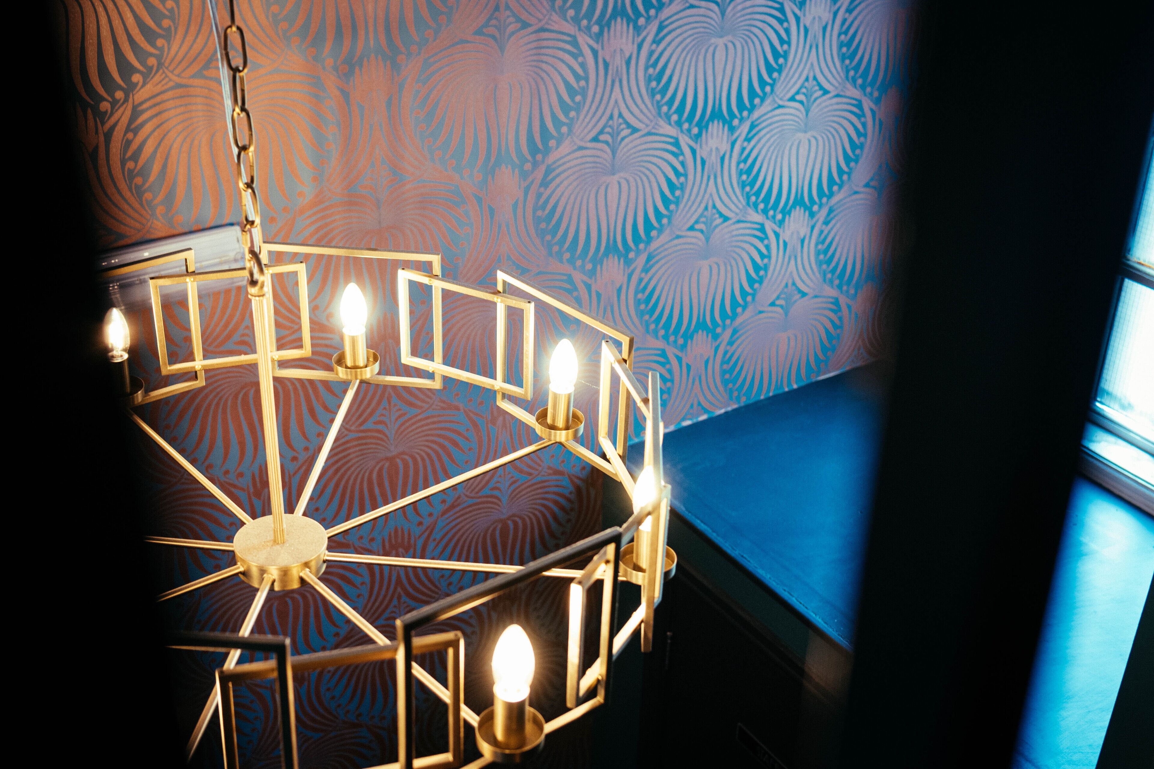 A chandelier with multiple light fixtures in a room with patterned wallpaper and a blue accent wall.