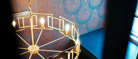 A chandelier with multiple light fixtures in a room with patterned wallpaper and a blue accent wall.