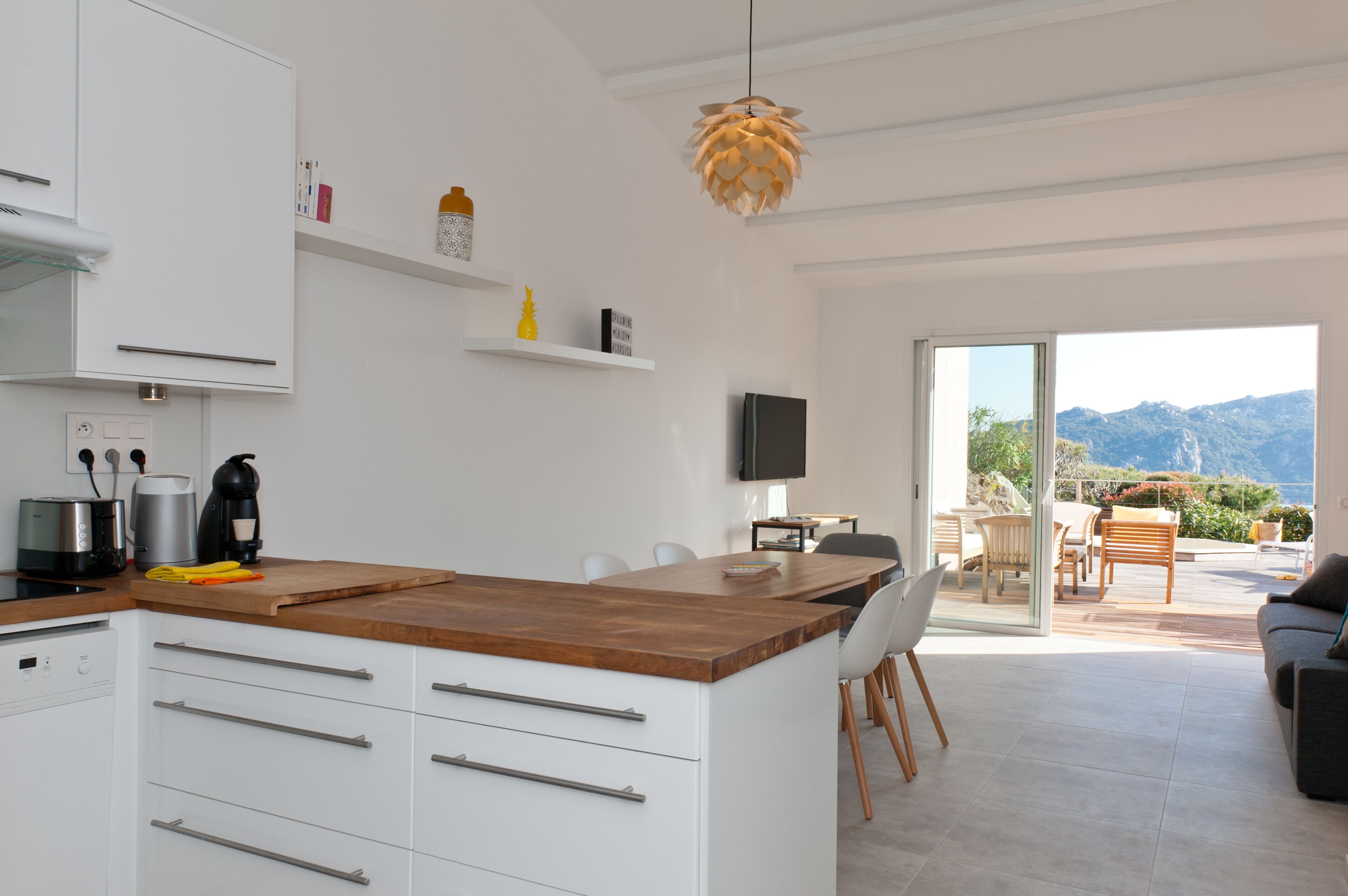 Una cocina moderna con armarios blancos, una encimera de madera y un comedor con mesa y sillas.