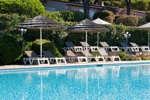 Un área de piscina con sillones de descanso y sombrillas de paja.