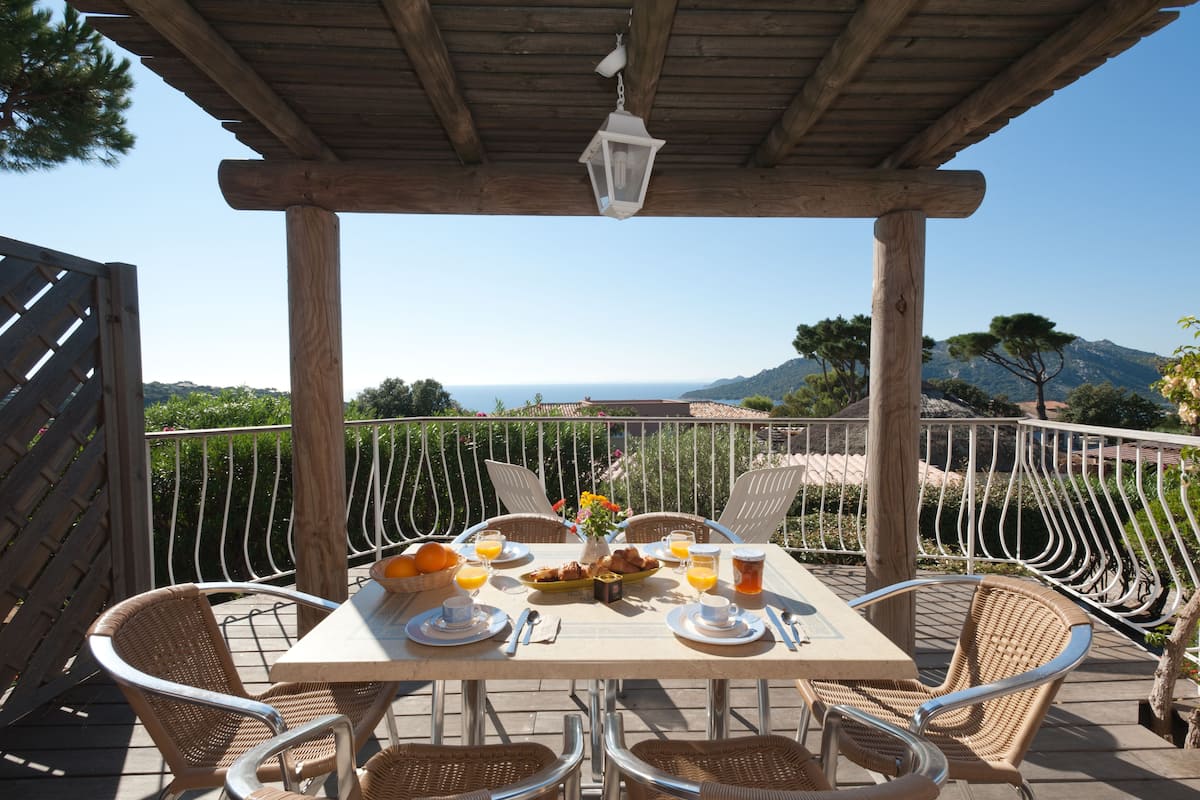 A wooden pergola with a table set for breakfast overlooking a scenic view.