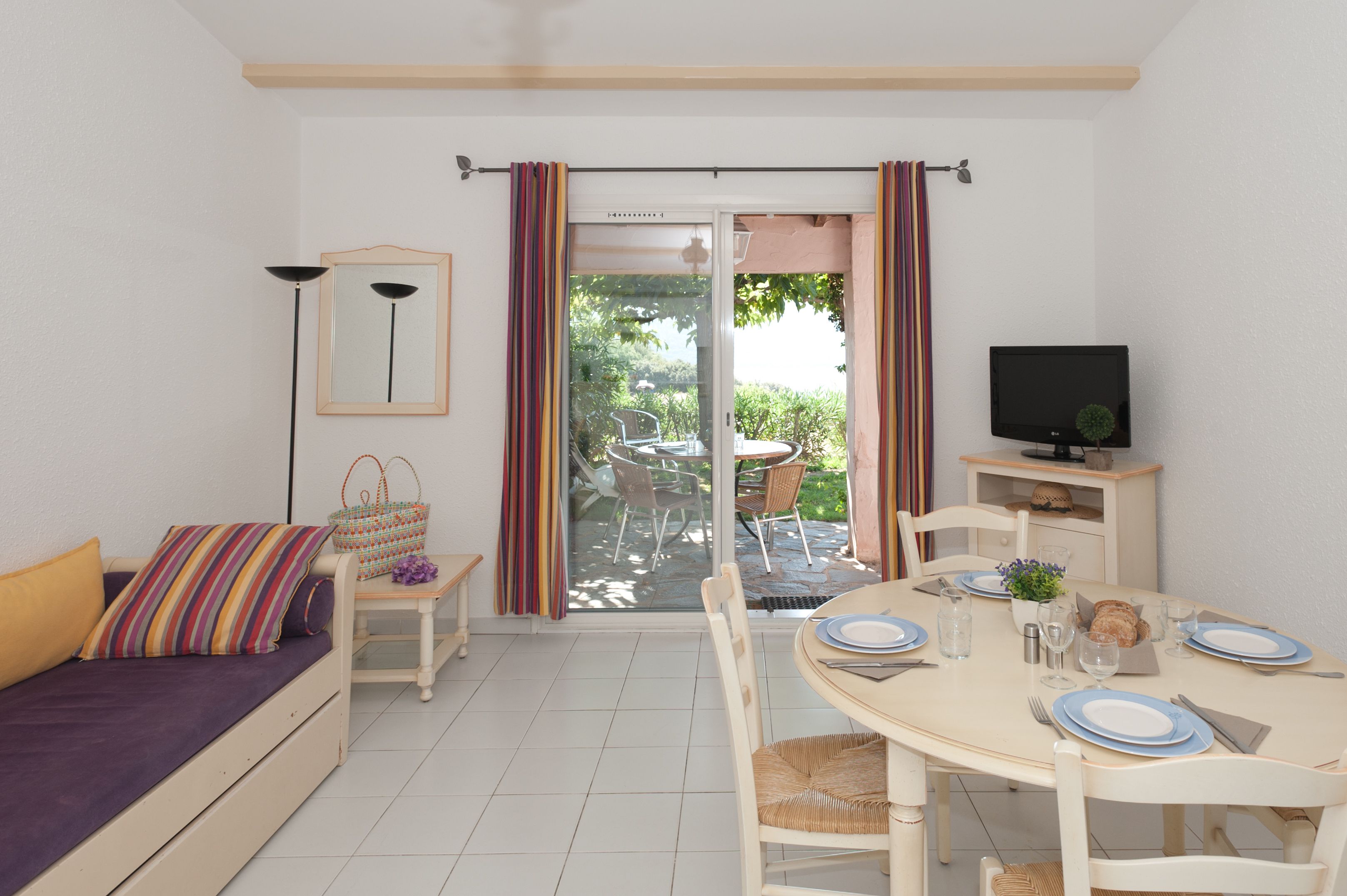 A cozy living room with a sofa, a dining table set for two, a television, and a sliding glass door leading to an outdoor area.
