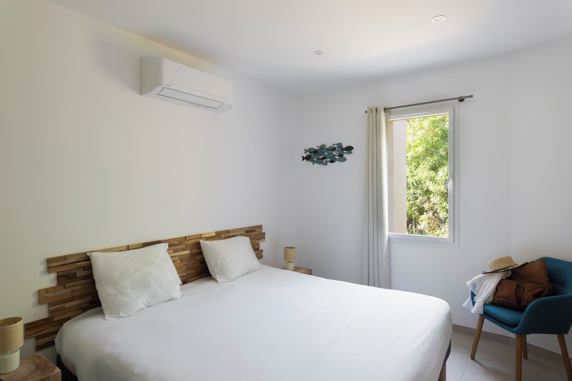 A bedroom with a bed, a window, a chair, and a wall-mounted air conditioner.
