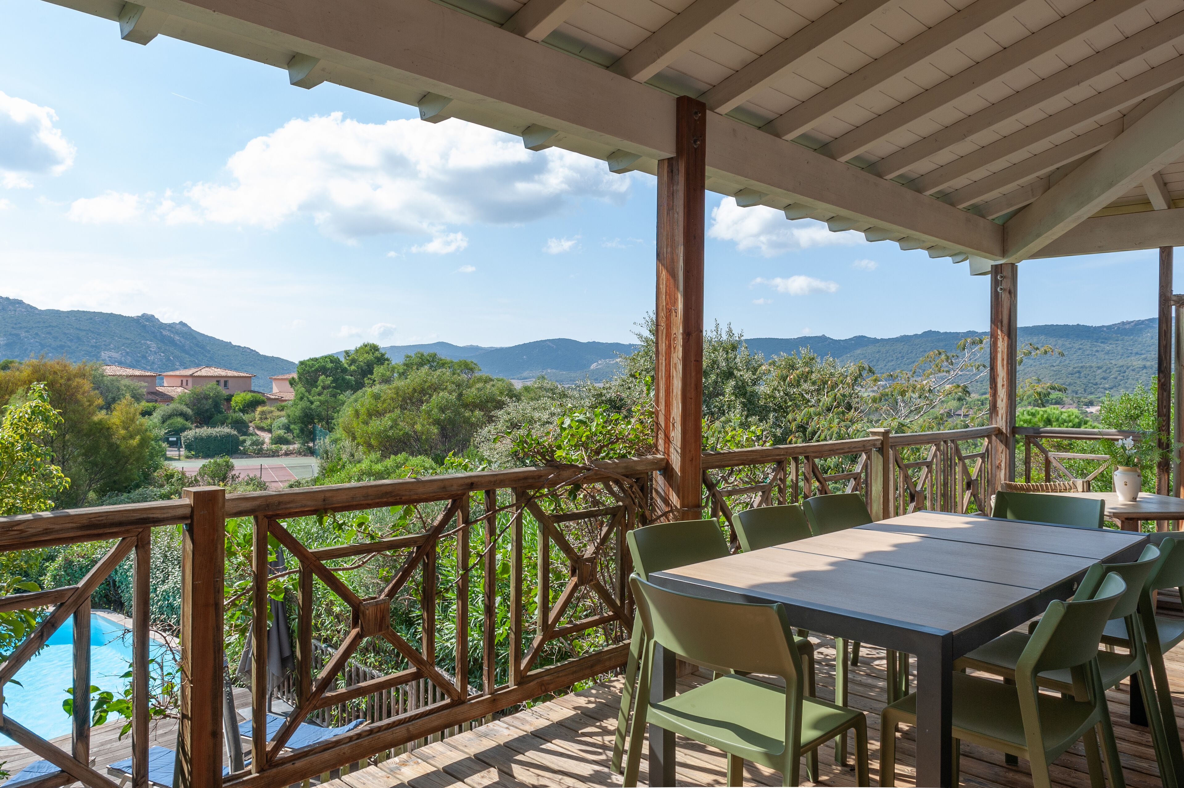 Uma área externa coberta com deck de madeira, piscina e mesa com cadeiras.