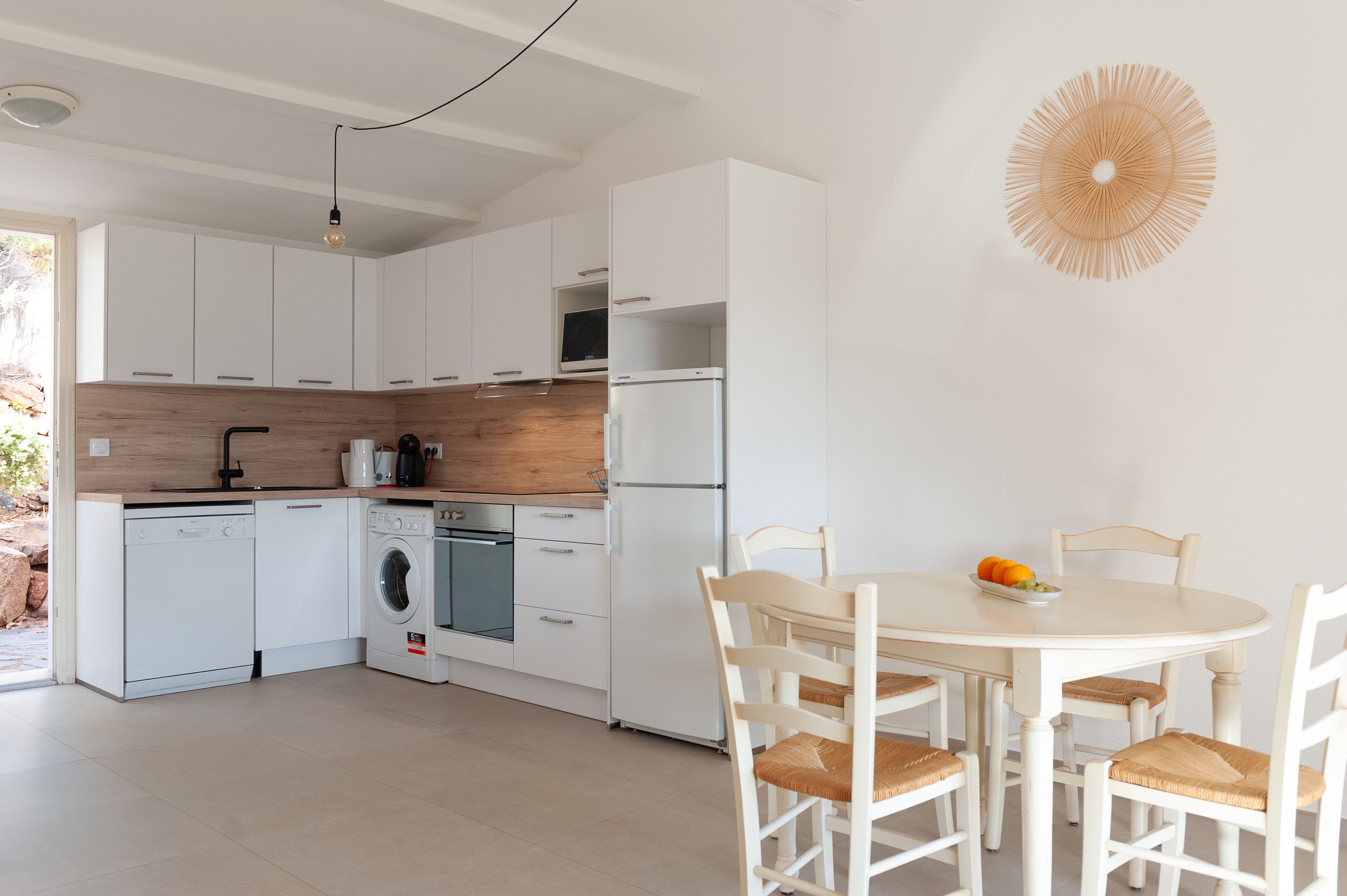 Una cucina moderna con mobili bianchi, lavastoviglie, lavatrice e zona pranzo con tavolo rotondo e sedie.