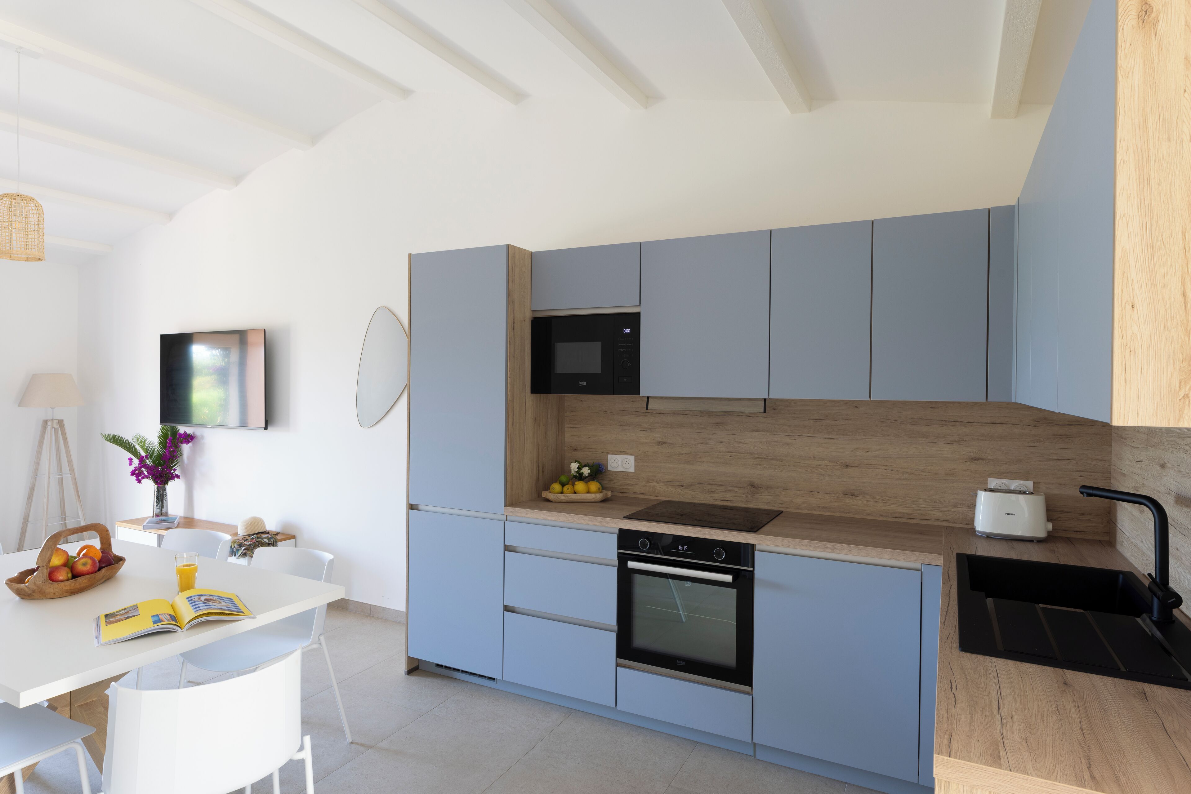 Een moderne keuken met lichtblauwe kastjes, een houten aanrecht, een magnetron, een oven en een spoelbak.
